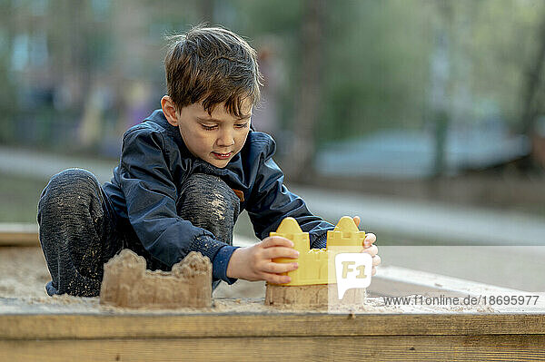 Boy building sandcastle with toy at park