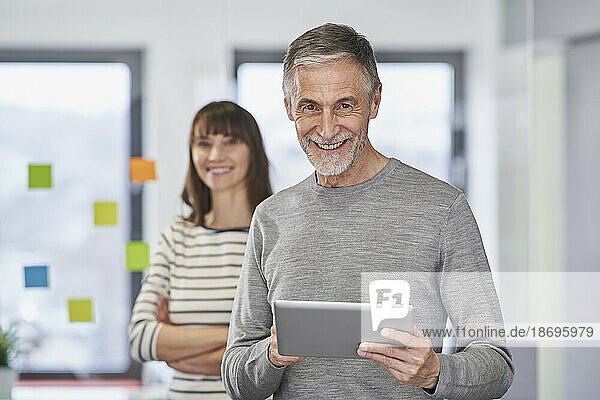 Smiling senior businessman holding tablet PC with colleague at workplace