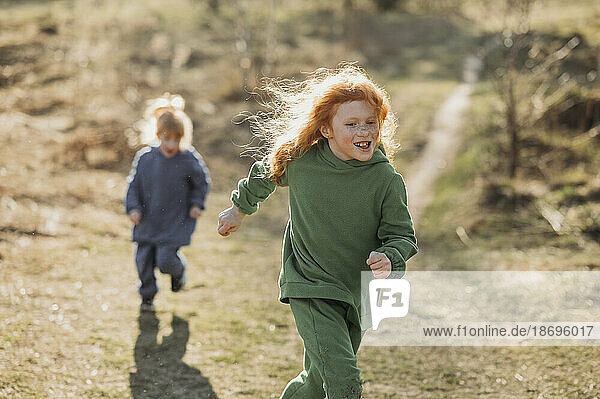 Happy siblings running in forest on sunny day