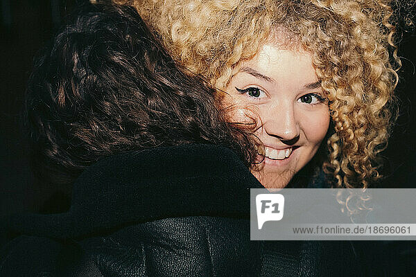 Smiling young woman with curly hair embracing friend