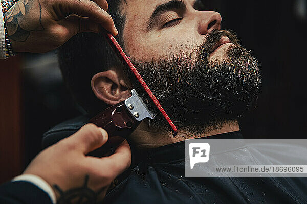 Customer with eyes closed getting beard trimmed in barber shop