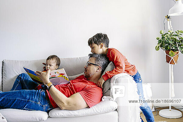 Vater liest Buch mit Söhnen auf Sofa im Wohnzimmer zu Hause