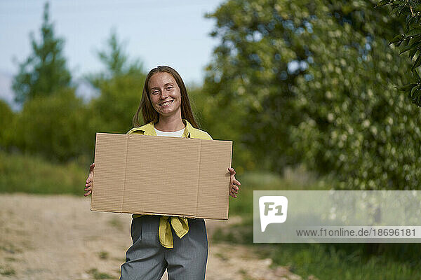 Lächelnde Frau hält leeren  ausgeschnittenen Karton im Garten