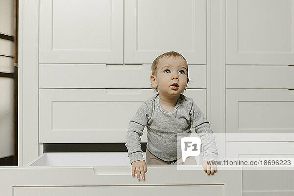Baby boy standing in drawer of wardrobe at home