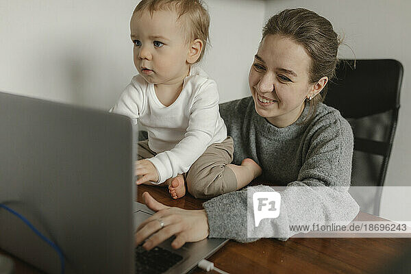 Lächelnde Mutter arbeitet mit ihrem kleinen Jungen im Heimbüro am Laptop