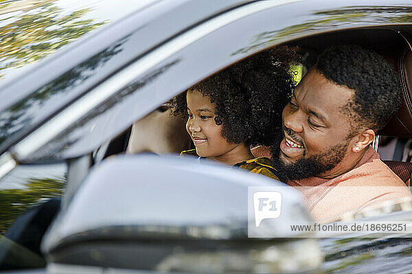 Smiling man enjoying road trip with daughter in car