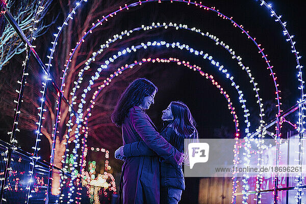 Mother and daughter embracing under illuminated Christmas lights