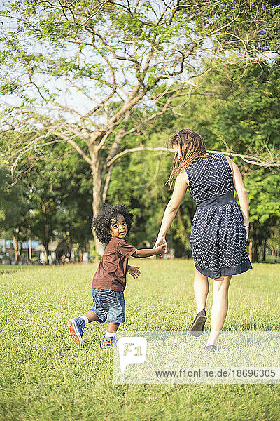 Mother and son holding hands and walking on grass at park