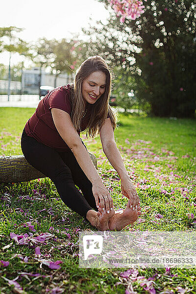 Smiling pregnant woman doing stretching exercise sitting on log on lawn