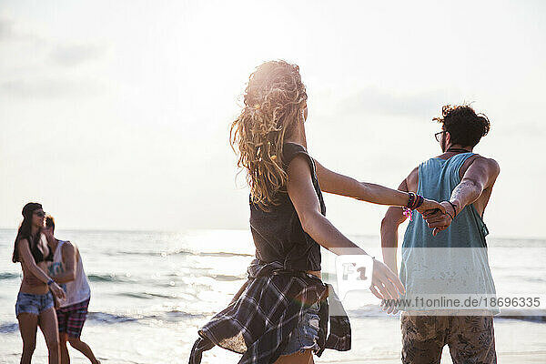 Carefree friends holding hands and playing at beach
