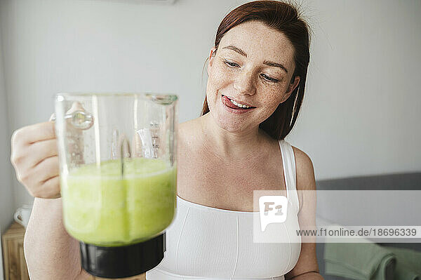 Pregnant woman holding pitcher of green smoothie at home