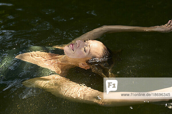 Smiling woman with eyes closed floating on water in lake