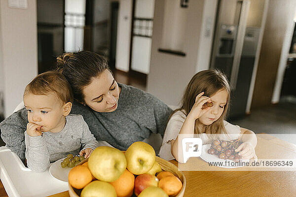 Mother with son and daughter eating fresh fruit at home