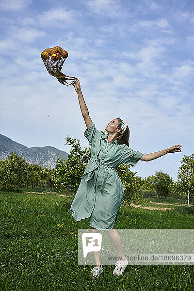 Playful woman with mesh bag in orange orchard
