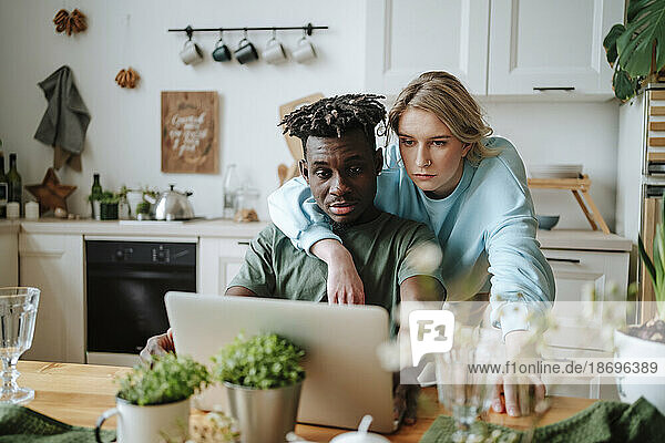 Young man sharing laptop with girlfriend in kitchen at home