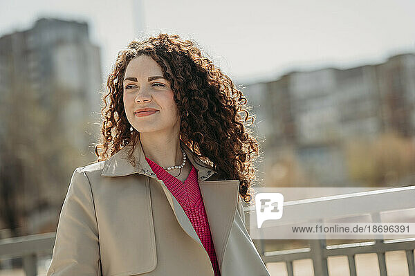 Smiling woman with curly hair contemplating at sunny day