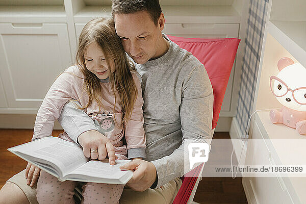 Girl sitting with father reading book at home