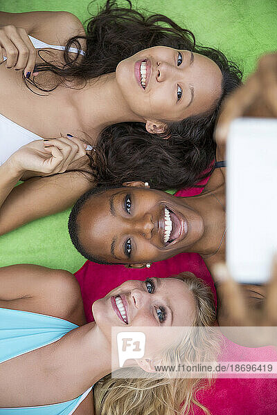 Happy women taking selfie lying on colorful blanket