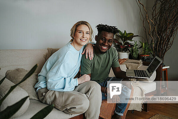 Smiling couple sitting with laptop in living room at home