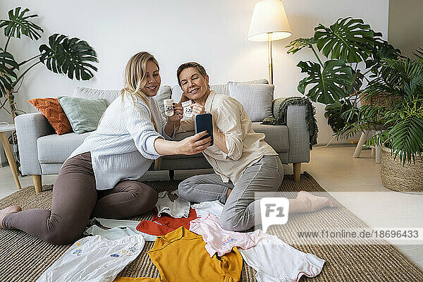 Pregnant daughter taking selfie with mother holding baby socks sitting at home