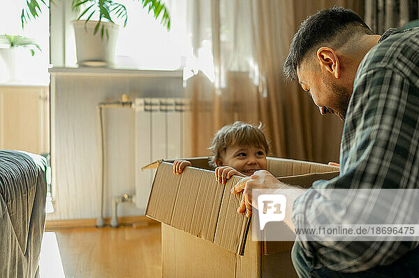 Vater spielt mit Sohn  der zu Hause im Karton sitzt