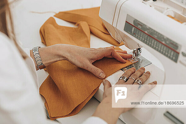 Seamstress sewing fabric through machine at workshop