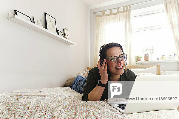 Thoughtful freelancer with laptop lying on bed at home