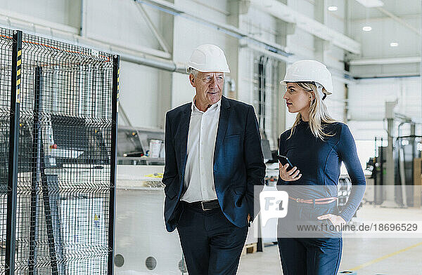 Colleague discussing with businessman walking in factory