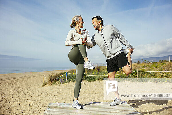 Happy mature couple stretching legs at beach