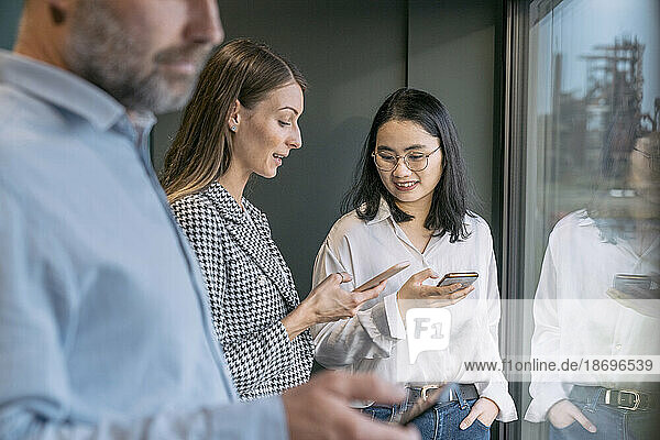 Businesswoman sharing mobile phone with colleague at the window