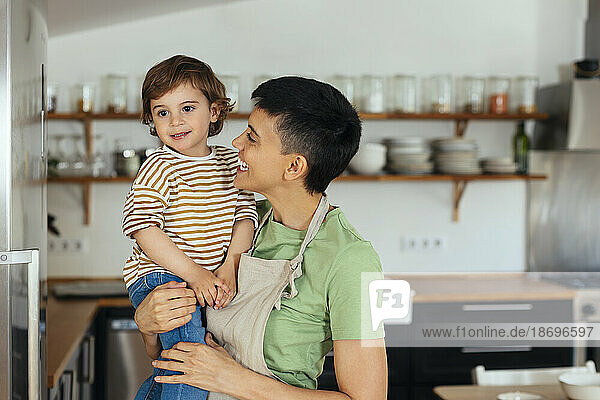 Happy woman carrying son in kitchen at home