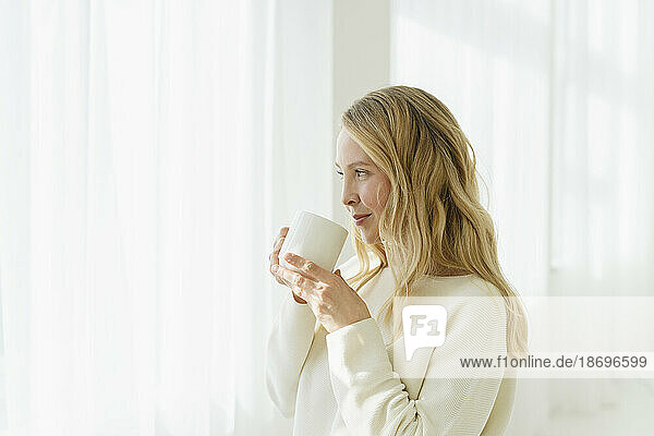Lächelnde Frau trinkt Kaffee vor einem durchscheinenden Vorhang