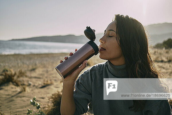 Woman with eyes closed drinking water from bottle at beach
