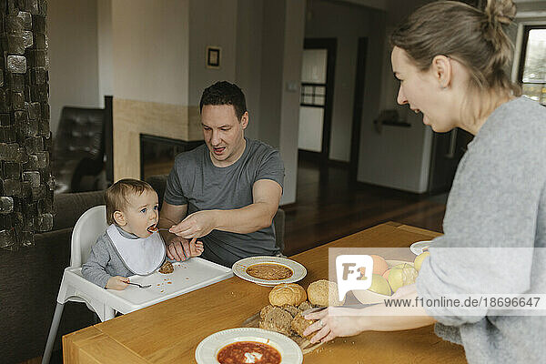 Father feeding baby boy at dining table at home