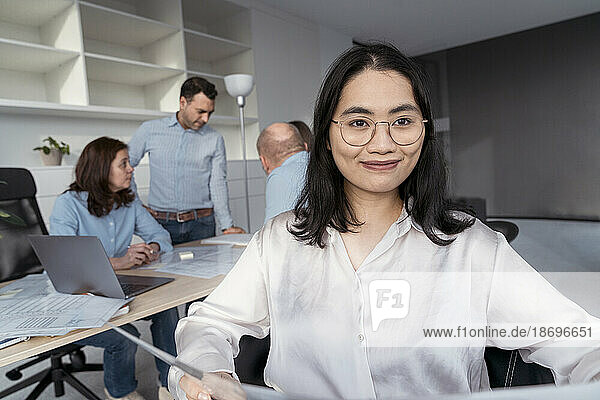 Confident young businesswoman with colleagues in background in office