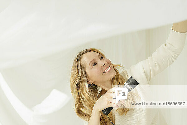 Smiling woman holding flashlight by translucent curtain