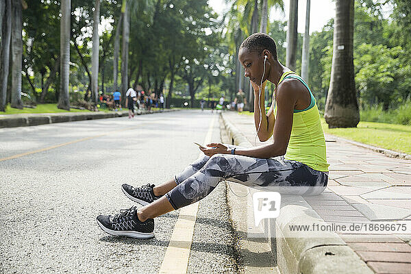 Frau sitzt auf Gehweg im Park und hört Musik