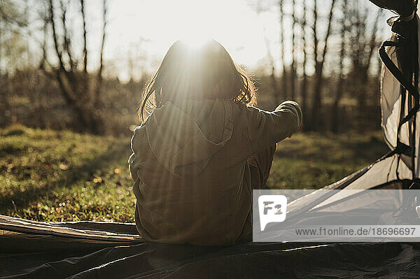Mädchen schaut an einem sonnigen Tag vom Zelt aus auf den Wald