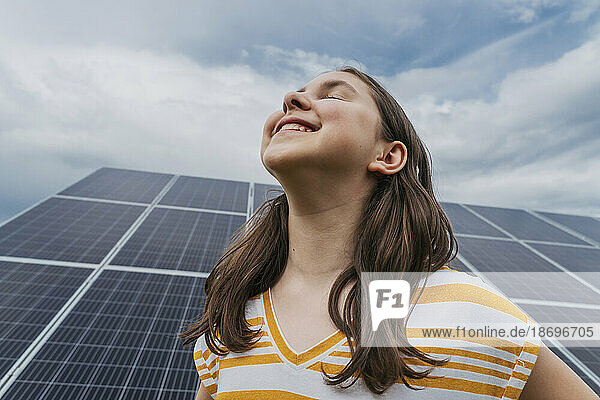 Lächelndes Mädchen mit geschlossenen Augen vor Sonnenkollektoren