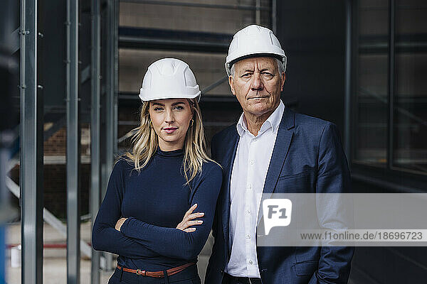 Confident businesswoman with arms crossed standing with businessman in factory