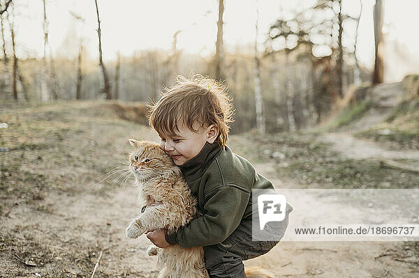 Boy playing with cat in forest at sunset