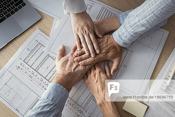 Business people stacking hands on desk with architectural plans