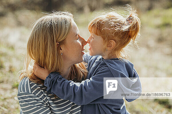 Mother and daughter rubbing noses on sunny day