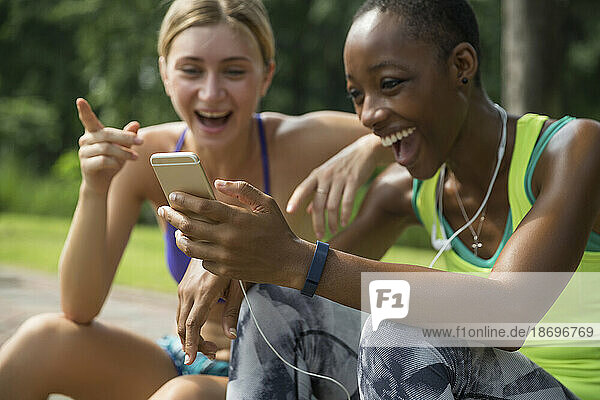 Fröhliche Freunde in Sportkleidung teilen sich im Park ihr Smartphone