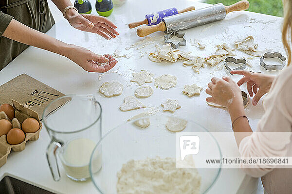 Mother and daughter making different shapes from dough in kitchen at home