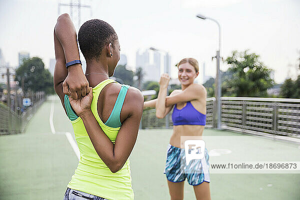 Woman in sports clothing stretching with friend on footpath