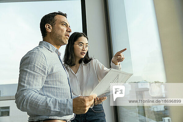 Geschäftsmann und Geschäftsfrau mit Architekturplan  der aus dem Fenster schaut