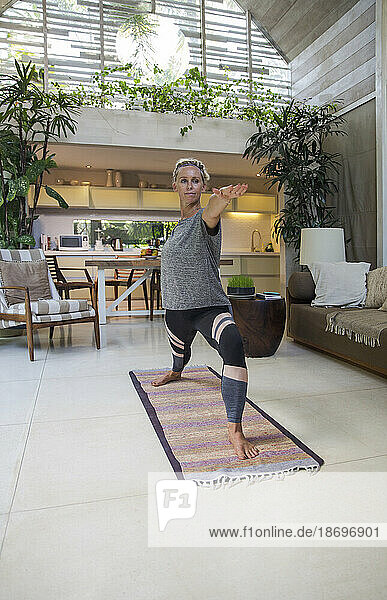 Woman practicing Warrior 2 pose on exercise mat at home