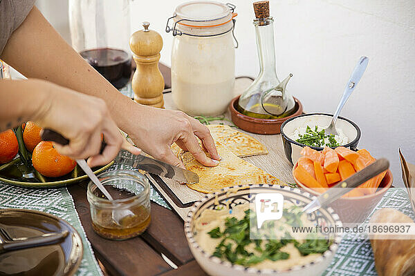 Hands cutting fermented bread surrounded with healthy meal in bowls and vegan products