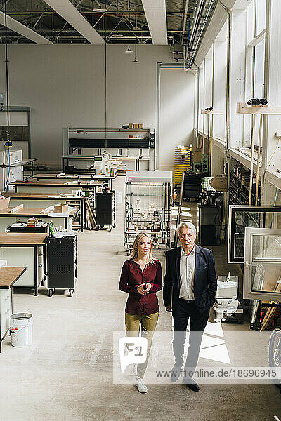 Businesswoman and businessman walking on production floor in factory
